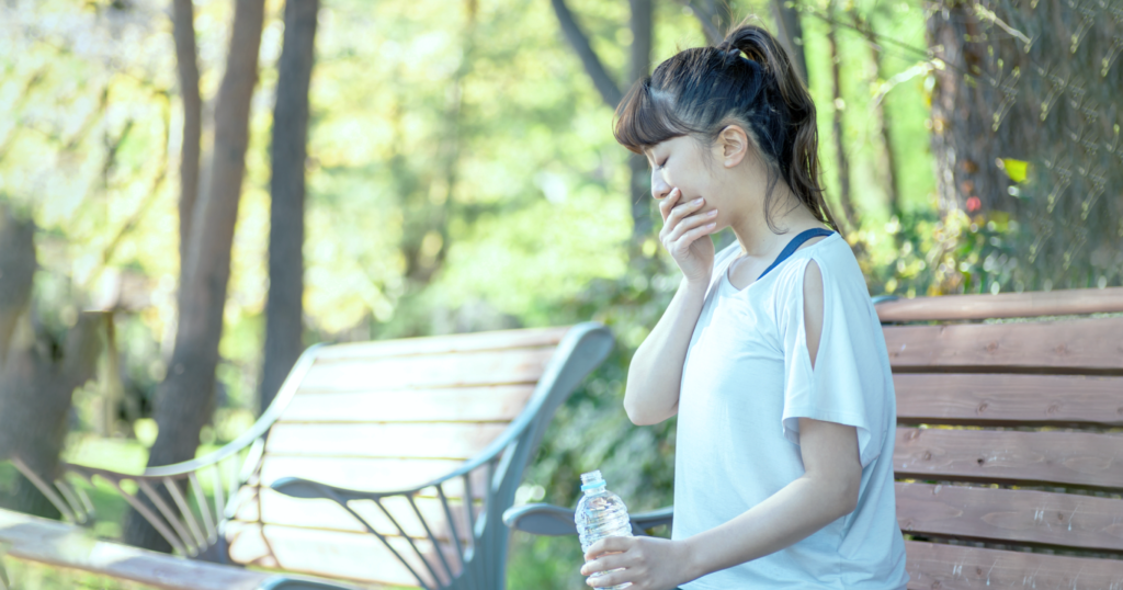 外のベンチで休む体調の悪い女性