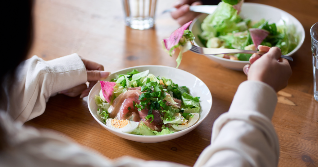 食卓で２人が向き合ってサラダを食している図