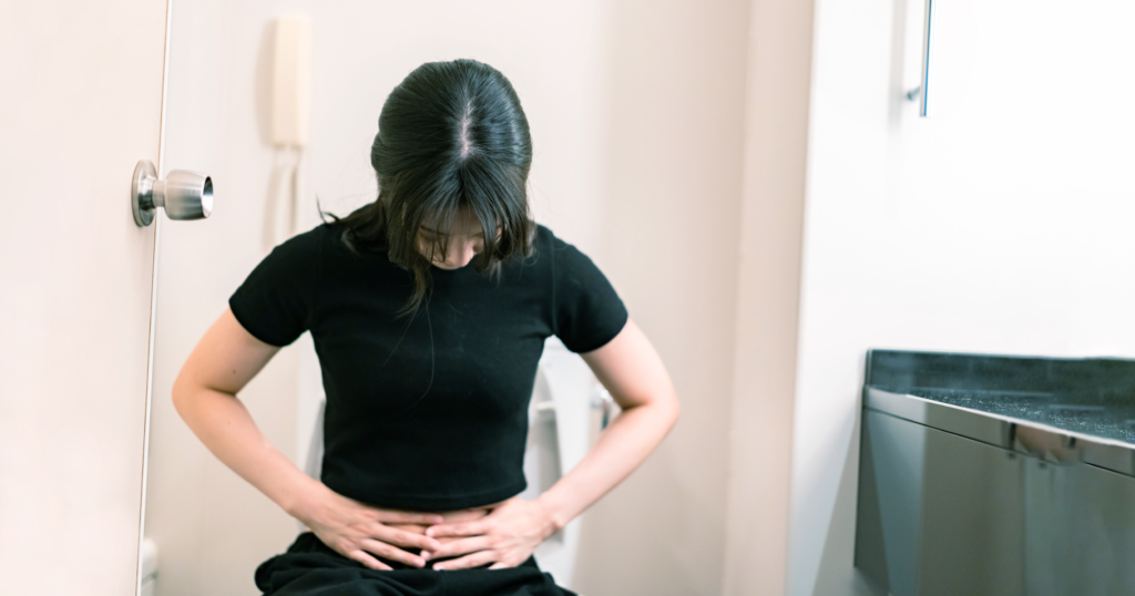 便座に座ってお腹を抑える女性