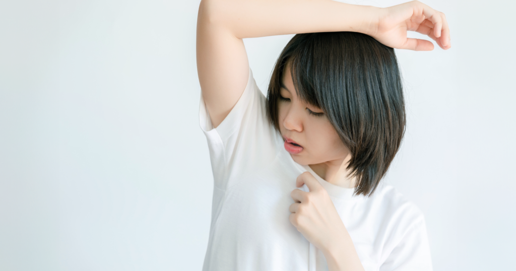 脇を広げてニオイを気にするTシャツ姿の女性