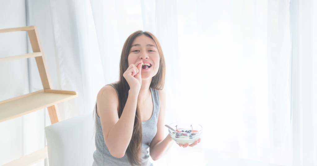 ベリーなどが入ったヨーグルトを片手に持ち、ベリーを食べる女性