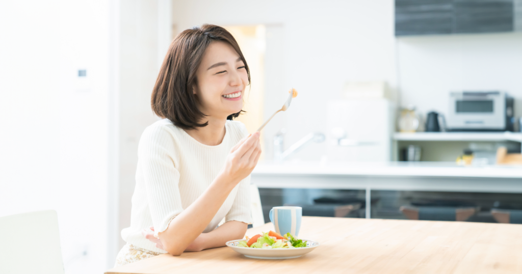 健康な女性がキッチンでサラダを笑顔で食べている画像
